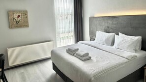 A modern hotel room with a large bed, white linens, a radiator, and a window with blinds. - Altınova Hotel Sakarya  (Serdivan)