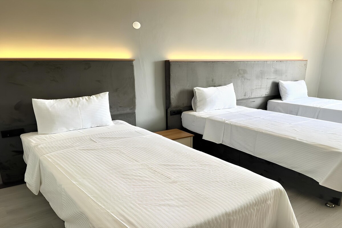 A hotel room with three single beds, a wooden nightstand, and a modern headboard.