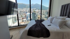A bedroom with a bed, a TV, and a city view through large windows. - Epiq Residences (Quito)