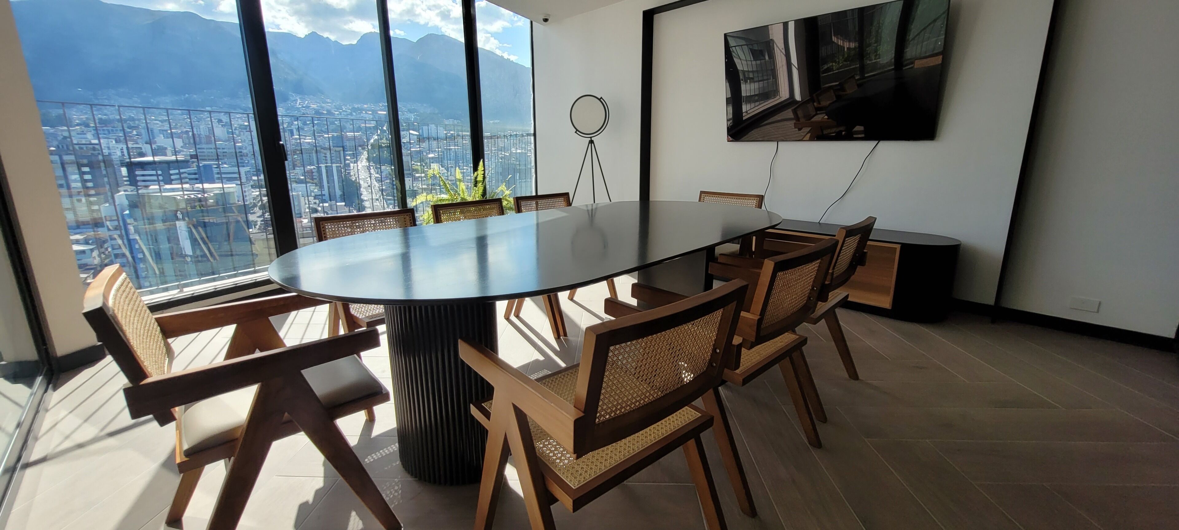Una sala de conferencias con una gran mesa redonda, seis sillas de madera con asientos de mimbre y un amplio ventanal con vistas a la ciudad.