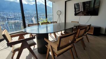Una sala de conferencias con una gran mesa redonda, seis sillas de madera con asientos de mimbre y un amplio ventanal con vistas a la ciudad.