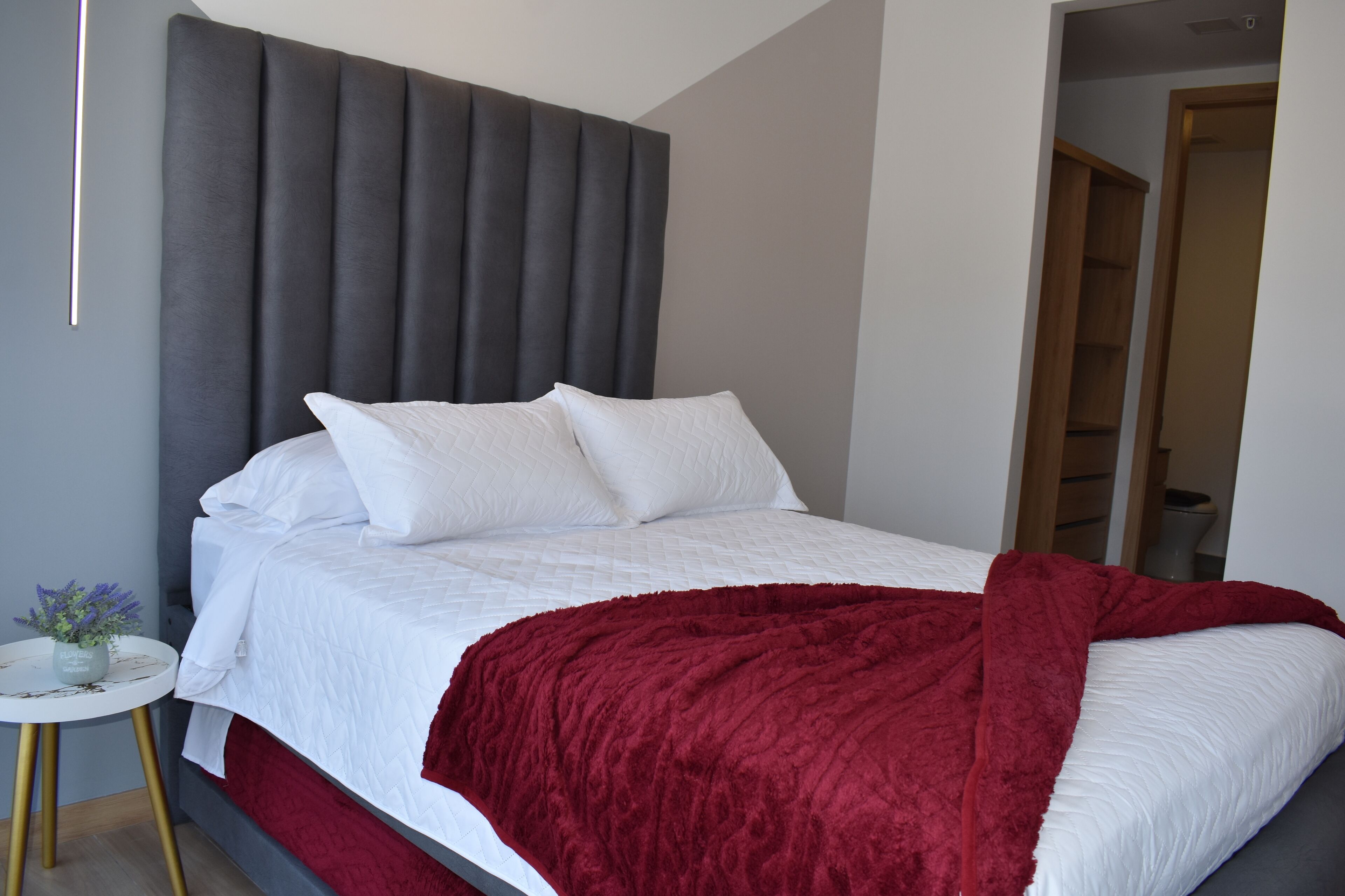 A modern bedroom with a large bed, a grey headboard, and a red throw blanket.