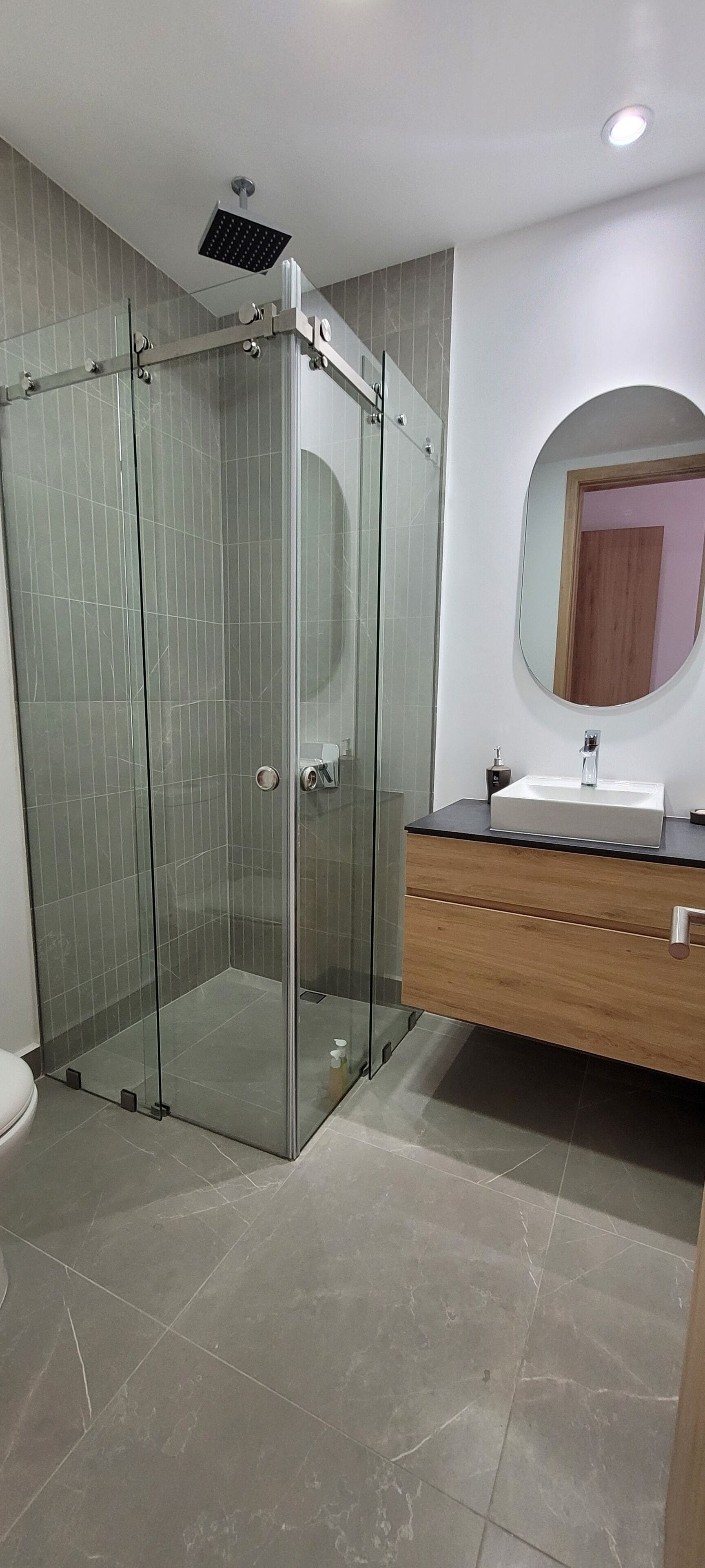 Un baño moderno con cabina de ducha de vidrio, tocador de madera con lavamanos y espejo.