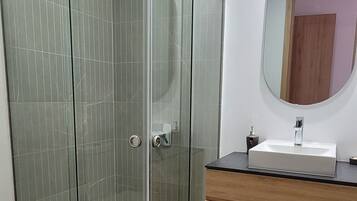 Un baño moderno con cabina de ducha de vidrio, tocador de madera con lavamanos y espejo.