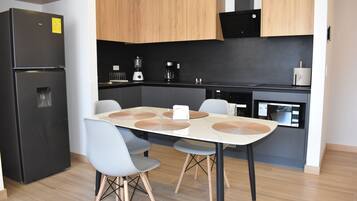A modern kitchen with a black refrigerator, wooden cabinets, a dining table with chairs, and a microwave.