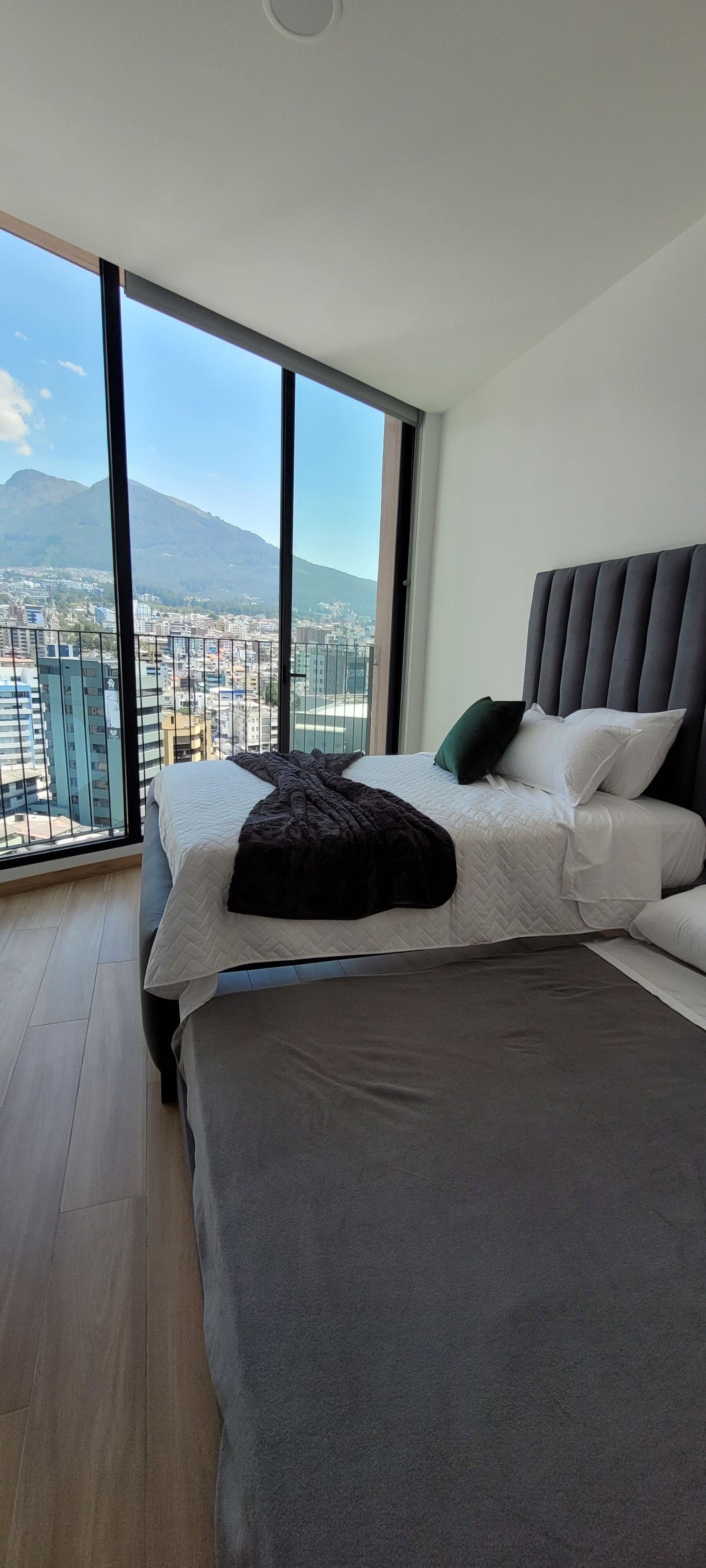 A bedroom with a large bed, a view of a cityscape, and a mountain in the background.