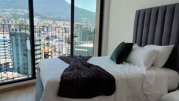 Un dormitorio con una cama grande, vistas a un paisaje urbano y una montaña al fondo.
