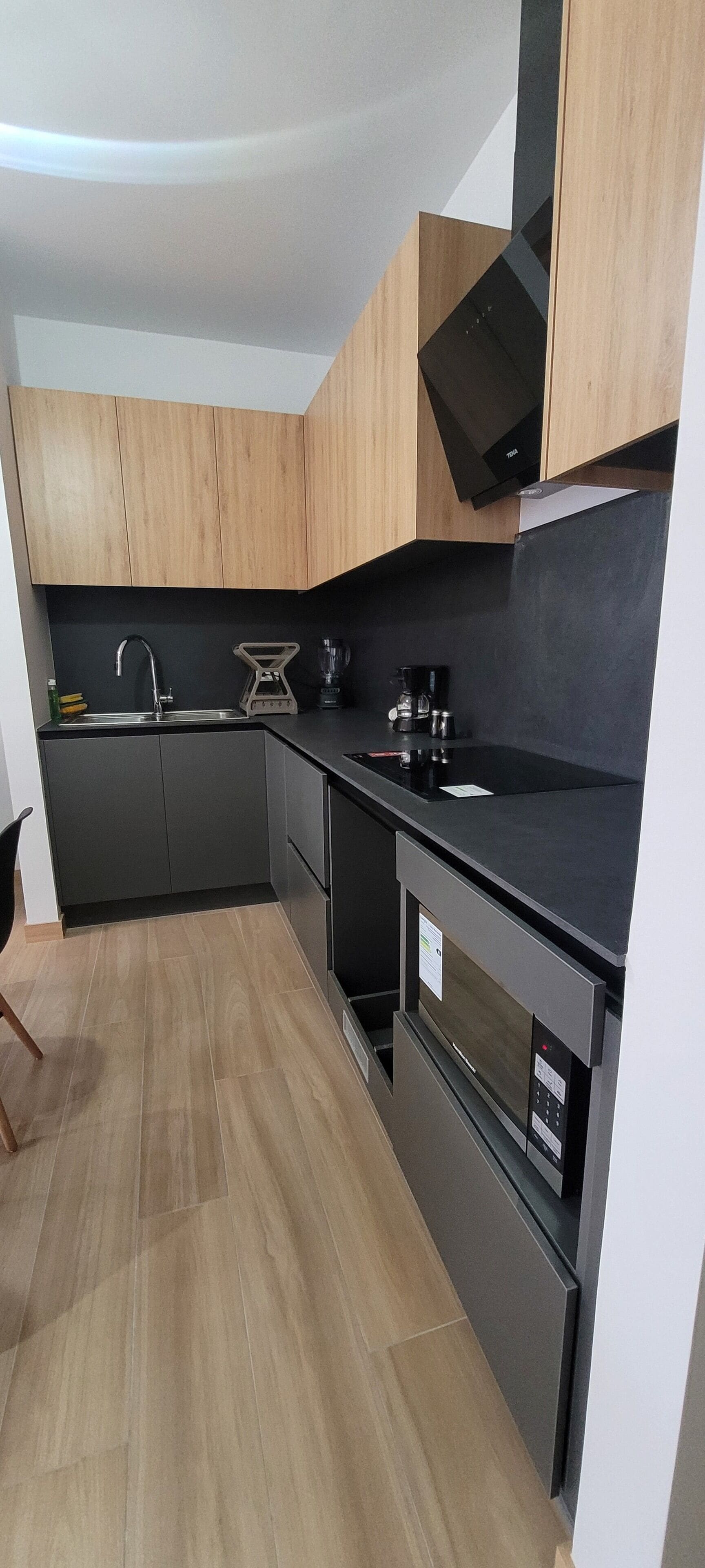 A compact kitchen with dark cabinetry, a black countertop, and a stainless steel range hood.