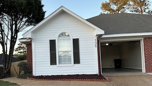 A single-story house with a garage, a front yard with a small garden, and a clear sky. - The Tiled Waters Retreat (Brandon)