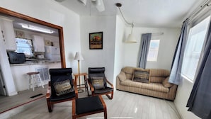 A living room with a sofa, two armchairs, a small table, and a kitchen in the background.