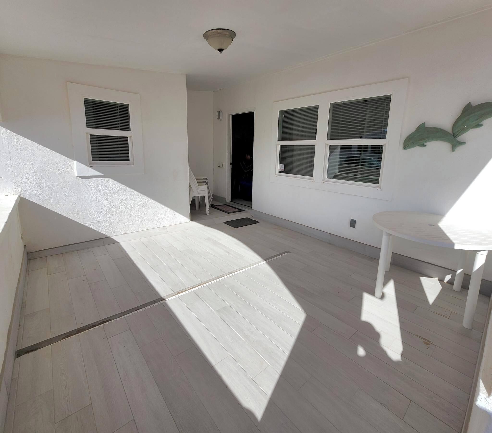A spacious room with a sloped ceiling, large windows with blinds, a white ceiling fan, and a small white table.
