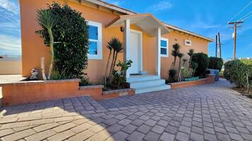 A two-story house with a paved driveway, a front porch, and a small garden with various plants.