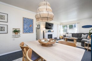 Una sala de estar moderna con comedor, que presenta una lámpara trenzada grande, un televisor de pantalla plana y un conjunto de asientos confortable.