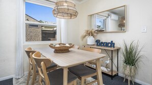 A dining area with a wooden table and chairs, a woven pendant light, a mirror, and a 'Beach' sign.