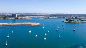A marina with multiple sailboats anchored in calm waters, surrounded by a coastal cityscape with buildings and greenery.