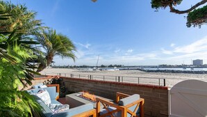 A patio with a fire pit, seating, and a view of the beach and boats.