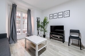 A living room with a white table, a black TV stand, a black chair, and a potted plant. - Modern and central apartment: Vibrant Lavapiés (Madrid)