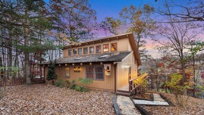 A wooden cabin with a sloped roof, multiple windows, and a porch with steps leading up to it.