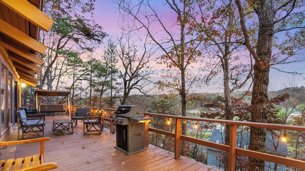 A wooden deck with outdoor seating, a grill, and a view of trees and buildings.