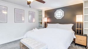 A modern bedroom with a large bed, a ceiling fan, and a bedside table with a lamp.