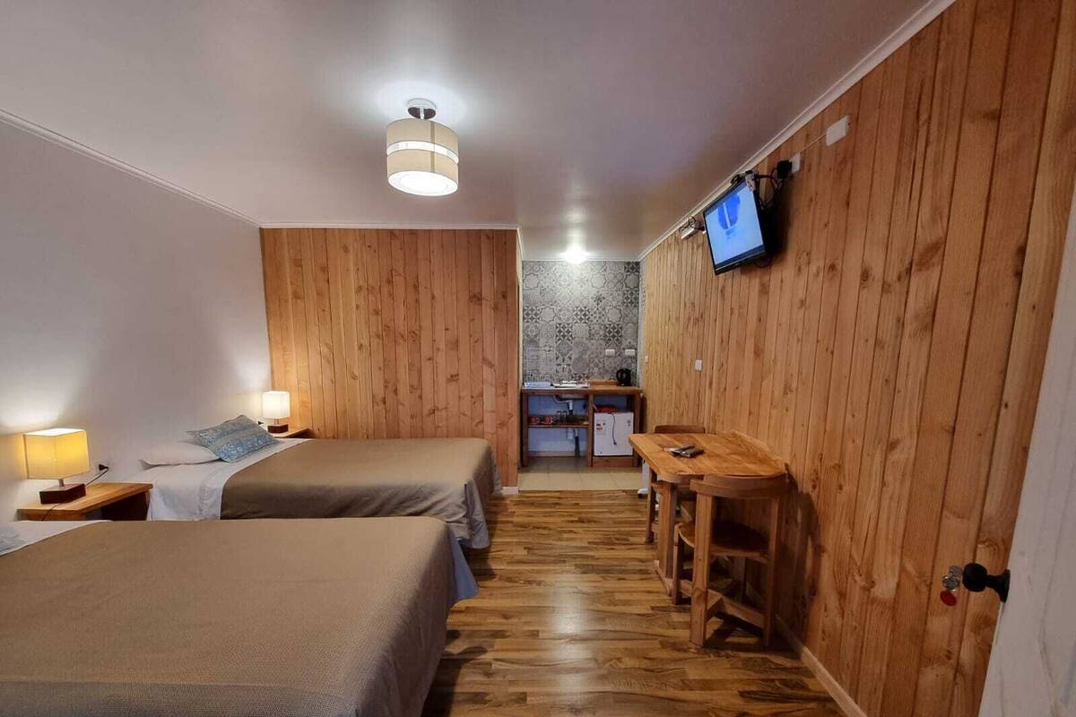Een kamer met twee bedden, een houten bureau, een televisie en een kitchenette.
