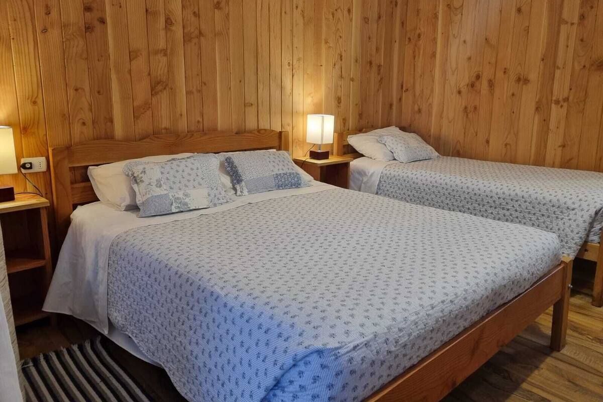 Een kamer met twee houten bedden, elk met een nachtkastje en een lamp.