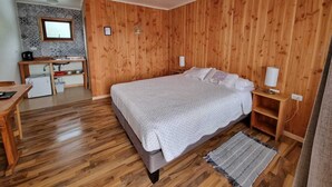 A bedroom with a wooden floor, a bed with white bedding, a wooden desk with a computer, and a small window. - Antu Apart Hotel Villarrica (Villarrica)