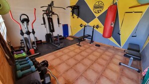 A gym with exercise equipment, a punching bag, and a wall with a fitness logo. - Antu Apart Hotel Villarrica (Villarrica)