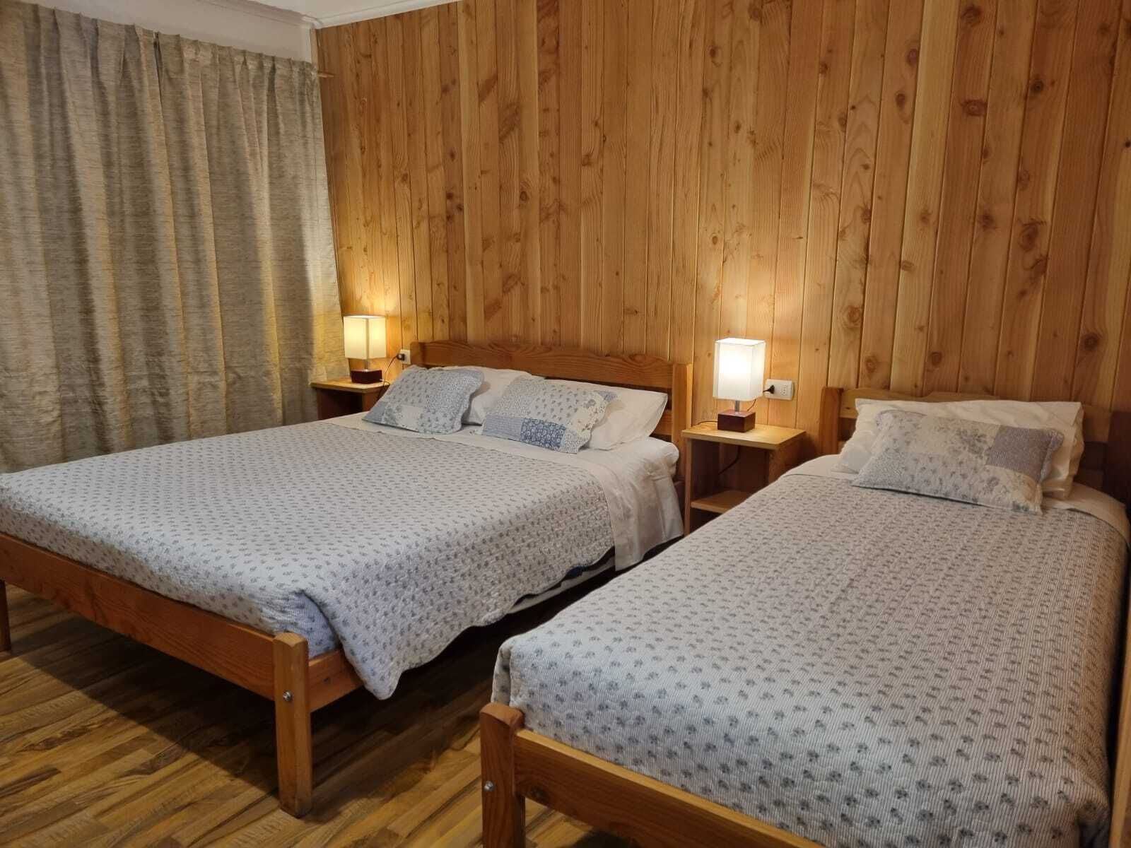 A room with two wooden beds, each with a nightstand and a lamp.