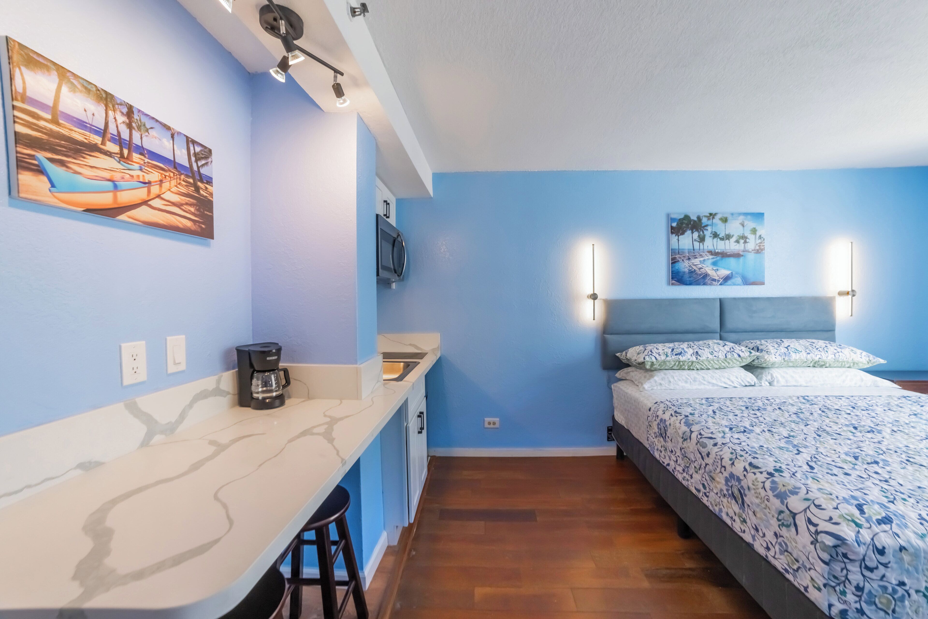 Une pièce comprenant un lit, un bureau et une chaise. Les murs sont ornés de tableaux et un luminaire est fixé au plafond.