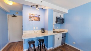 A compact kitchen with a marble countertop, a microwave, a coffee maker, and two stools. - Trendy Studio in the Heart of Honolulu - 21F  (Honolulu)