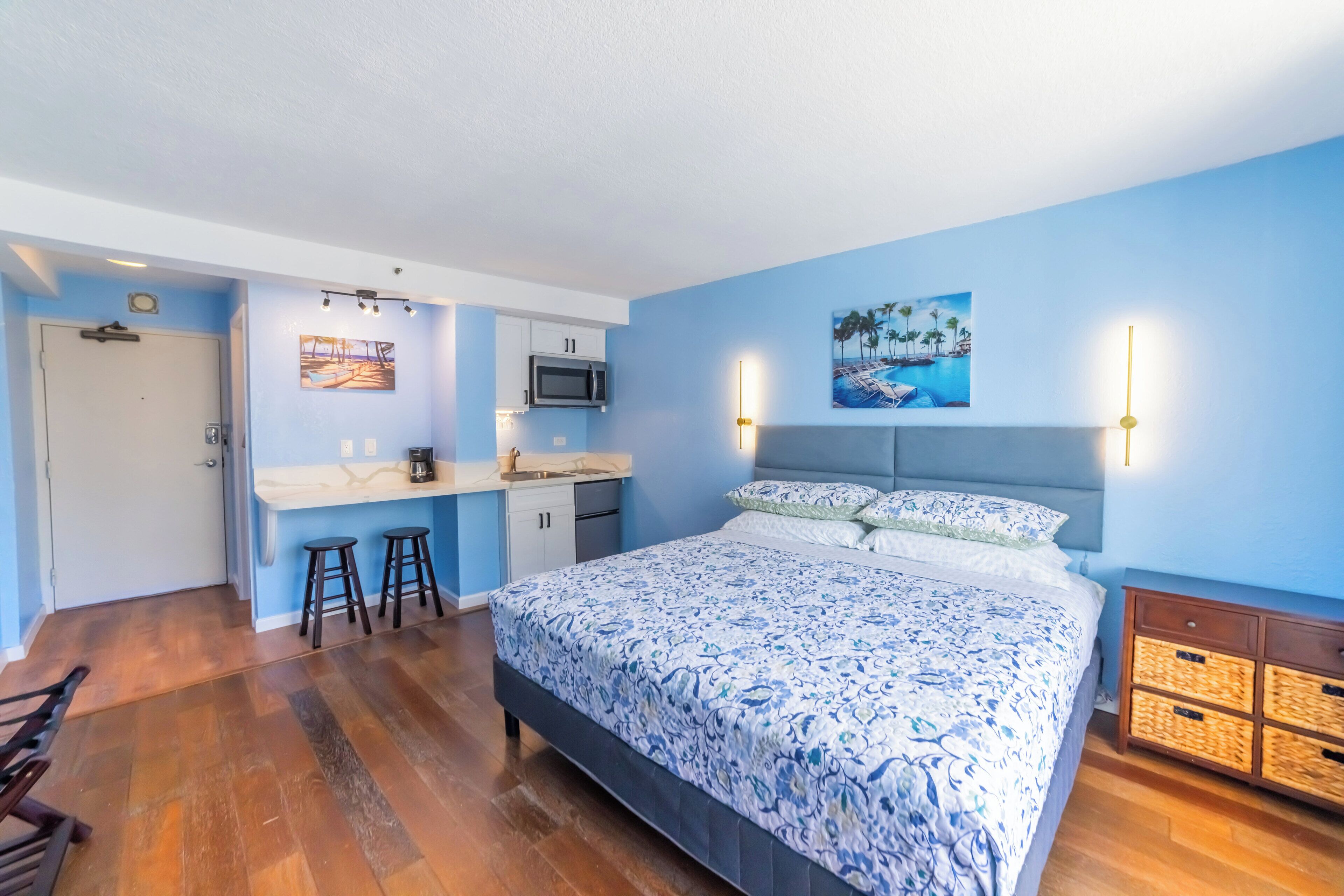A bedroom with a bed, a desk, and a kitchenette.