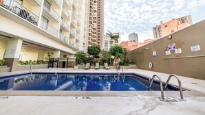 A swimming pool with a 5'1.5" depth, surrounded by a building with balconies and a clock on the wall. - Trendy Studio in the Heart of Honolulu - 21F  (Honolulu)