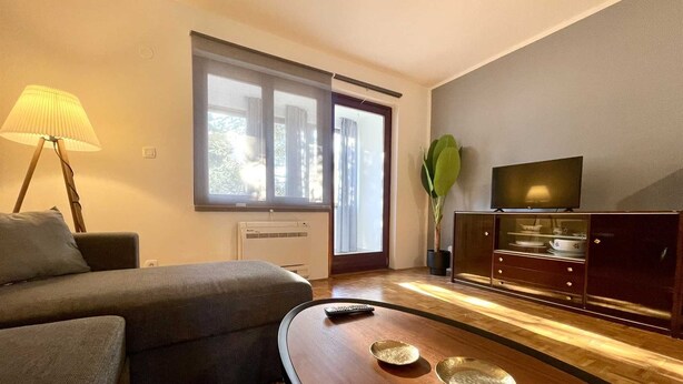 A modern living room with a sofa, a coffee table, a TV, and a large window.