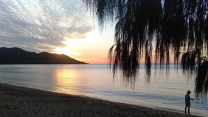 Ranta, jolla henkilö on kalastamassa, tyyni vesi ja auringonlasku taustalla.