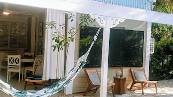 A covered outdoor seating area with a hammock, wooden chairs, and a table.