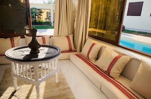 A modern living room with a white sofa, a round table, and a view of a swimming pool.
