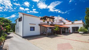 Une maison à deux étages, avec un toit en tuiles, une terrasse couverte et une cour dallée.