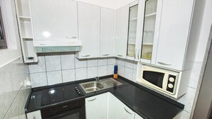 Une cuisine compacte avec des meubles blancs, un plan de travail noir, un four à micro-ondes encastré et une cuisinière.