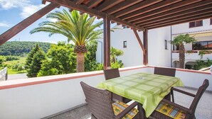 Un balcon avec une table et des chaises, donnant sur un paysage luxuriant, avec des palmiers et un bâtiment en arrière-plan.