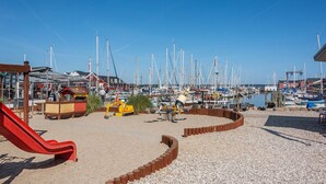 A marina with numerous boats docked, a playground with a red slide, and a sandy area with wooden structures. - Gorgeous home in Juelsminde with WiFi (Juelsminde)