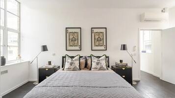 Een slaapkamer met een groot bed, twee nachtkastjes, een raam en twee ingelijste foto's aan de muur.