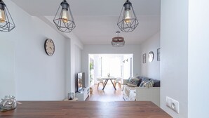 A modern kitchen with a wooden countertop, pendant lights, a clock, and a view to a dining area.