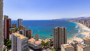 A coastal cityscape with high-rise buildings, a beach with umbrellas, and clear blue waters.