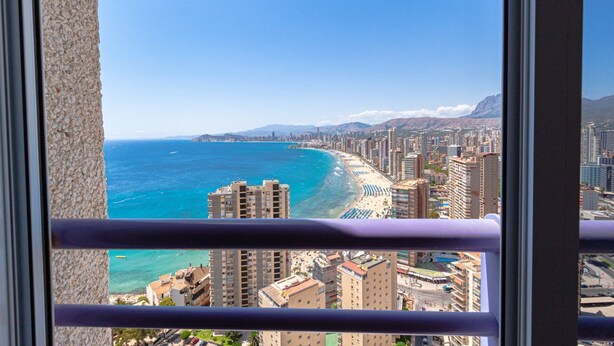 A coastal cityscape with high-rise buildings, a beach, and mountains in the distance.