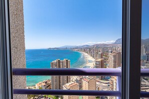 A coastal cityscape with high-rise buildings, a beach, and mountains in the distance.