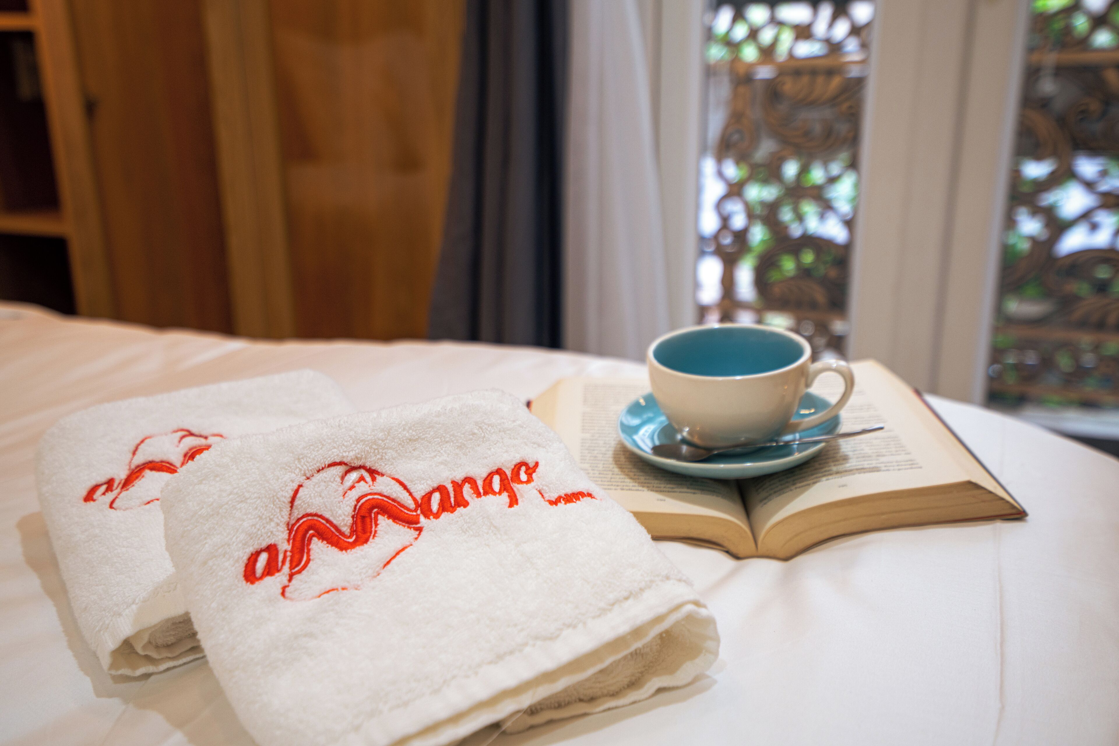 A neatly made bed with a folded towel, a cup of coffee, and an open book on a white bedspread.