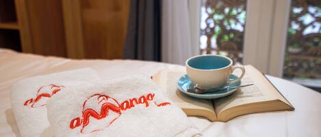 A neatly made bed with a folded towel, a cup of coffee, and an open book on a white bedspread.