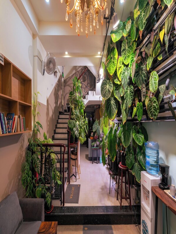 A cozy indoor space with a staircase, a bookshelf, and various potted plants.