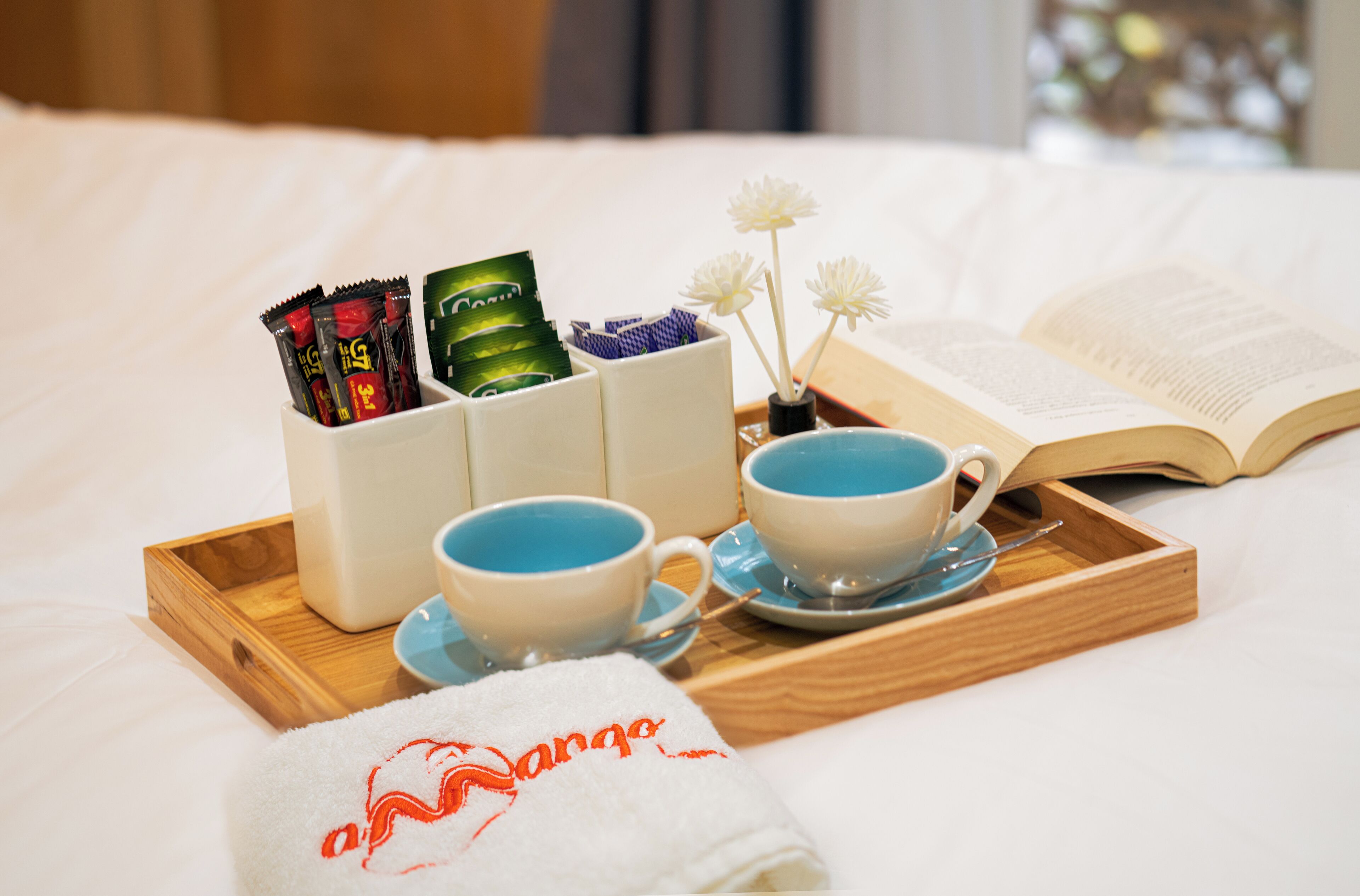 A neatly arranged breakfast tray on a bed with a book, a towel, and a container with snacks.